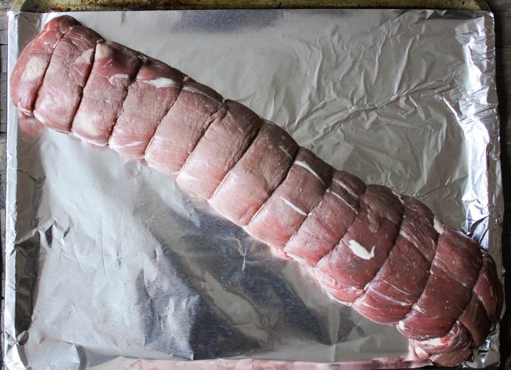 Whole raw beef tenderloin, trimmed and tied, on a foil-lined baking sheet.