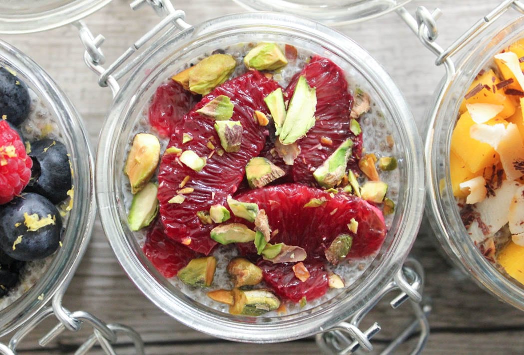 Overhead shot of garnished chia seed pudding in a small pot topped with blood orange segments and chopped pistachios.