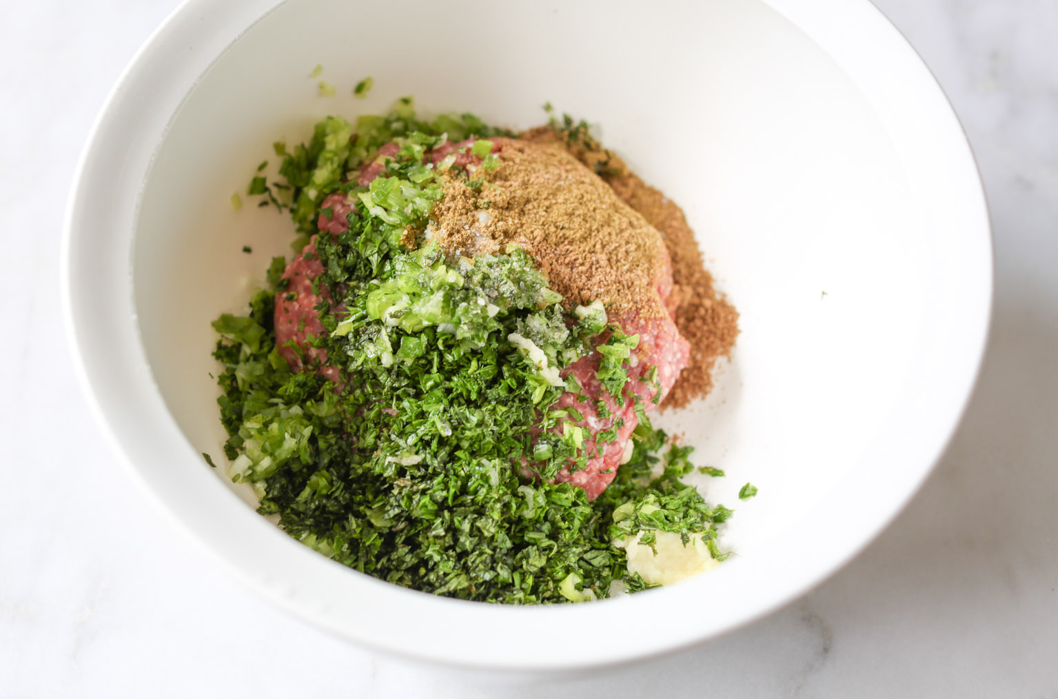 Overhead view of a mixing bowl with ingredients for spiced lamb meatballs.